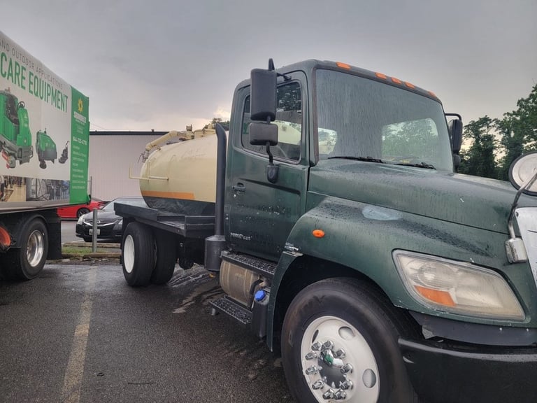 Green tanker truck parked in a lot with a care equipment sign visible in the background