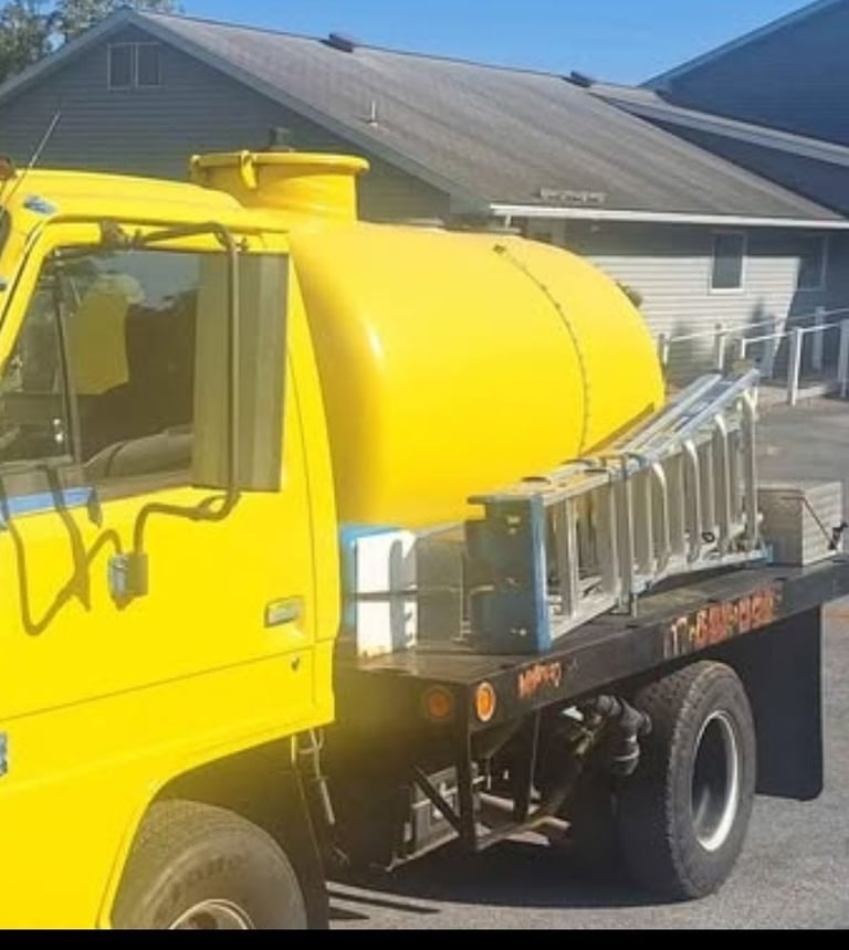 Bright yellow concrete mixer truck with cylindrical rotating drum parked in residential driveway