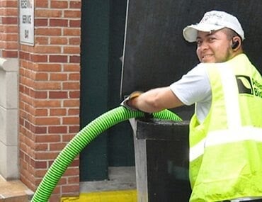 Worker in yellow safety vest and white cap holding a green hose near a brick wall